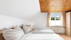 A bedroom with a bed, pillows, a nightstand, a window with curtains, and a view of trees.