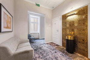 A hotel lobby with a sofa, a radiator, a door with intricate gold detailing, and a framed picture on the wall. - Kaiser 2BR | Metro & Tram | Nespresso | Central (Wien)