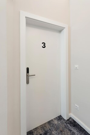 Eine weiße Tür mit der Nummer 3, ein moderner Türgriff und eine kleine Steckdose an der Wand.