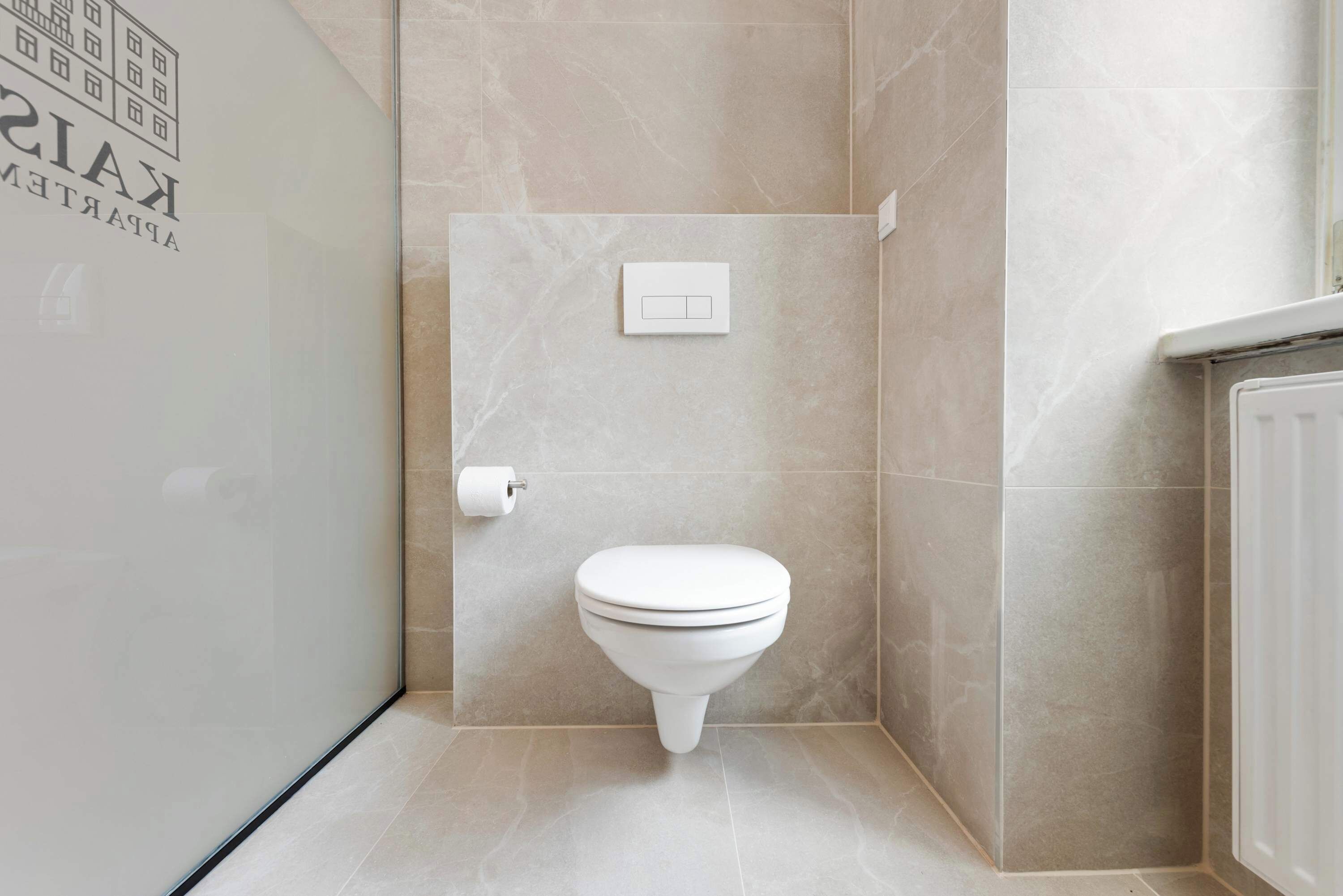Ein modernes Badezimmer mit Toilette, Seifenspender und Lichtschalter an der Wand.