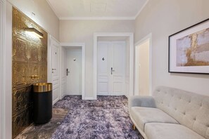 A hallway with a gold door, a black trash bin, a grey sofa, and a framed picture on the wall. - Kaiser 2BR | Metro & Tram | Nespresso | Central (Wien)