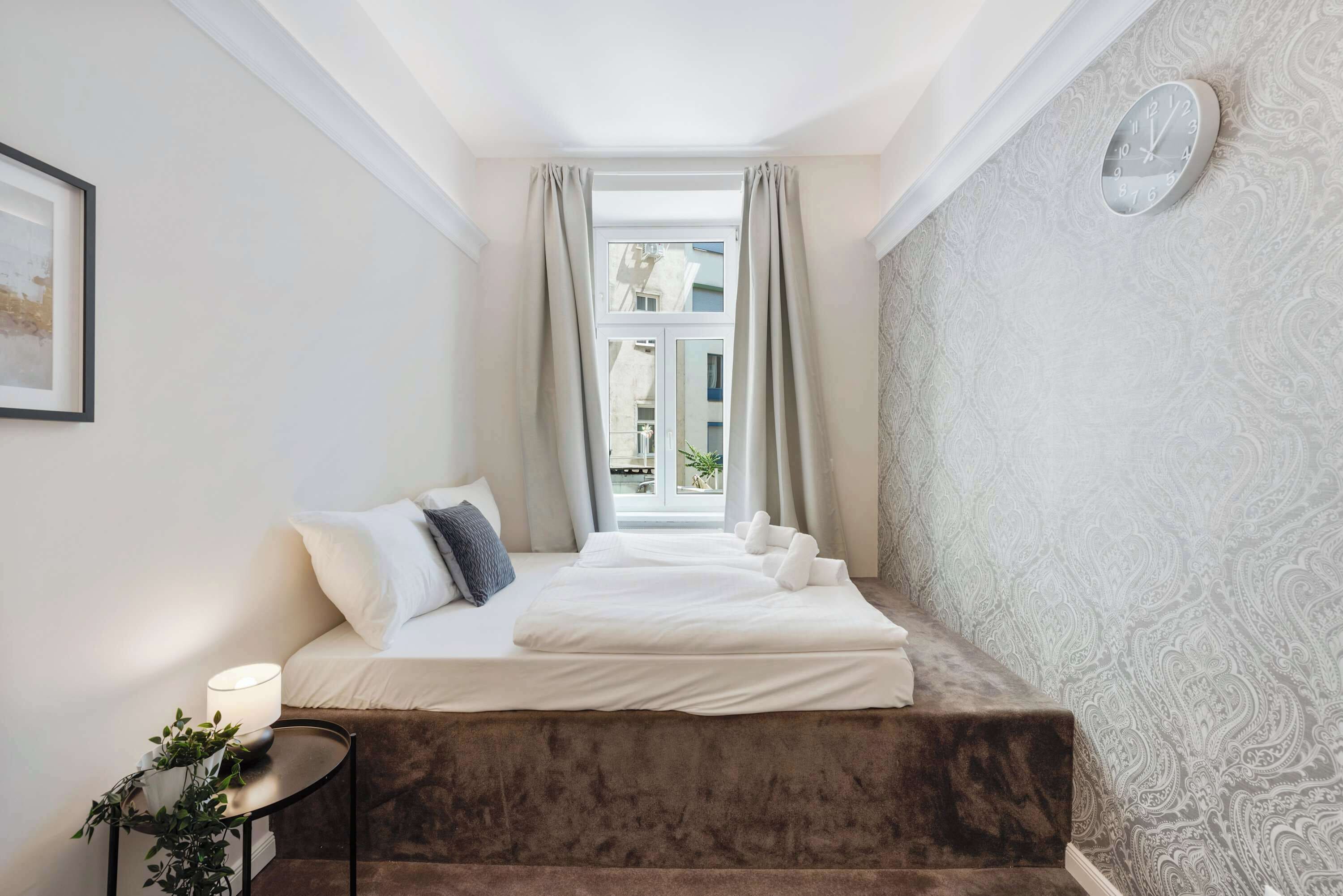 Une chambre d’hôtel avec un lit, une table de chevet, une lampe et une vue sur les bâtiments par la fenêtre.