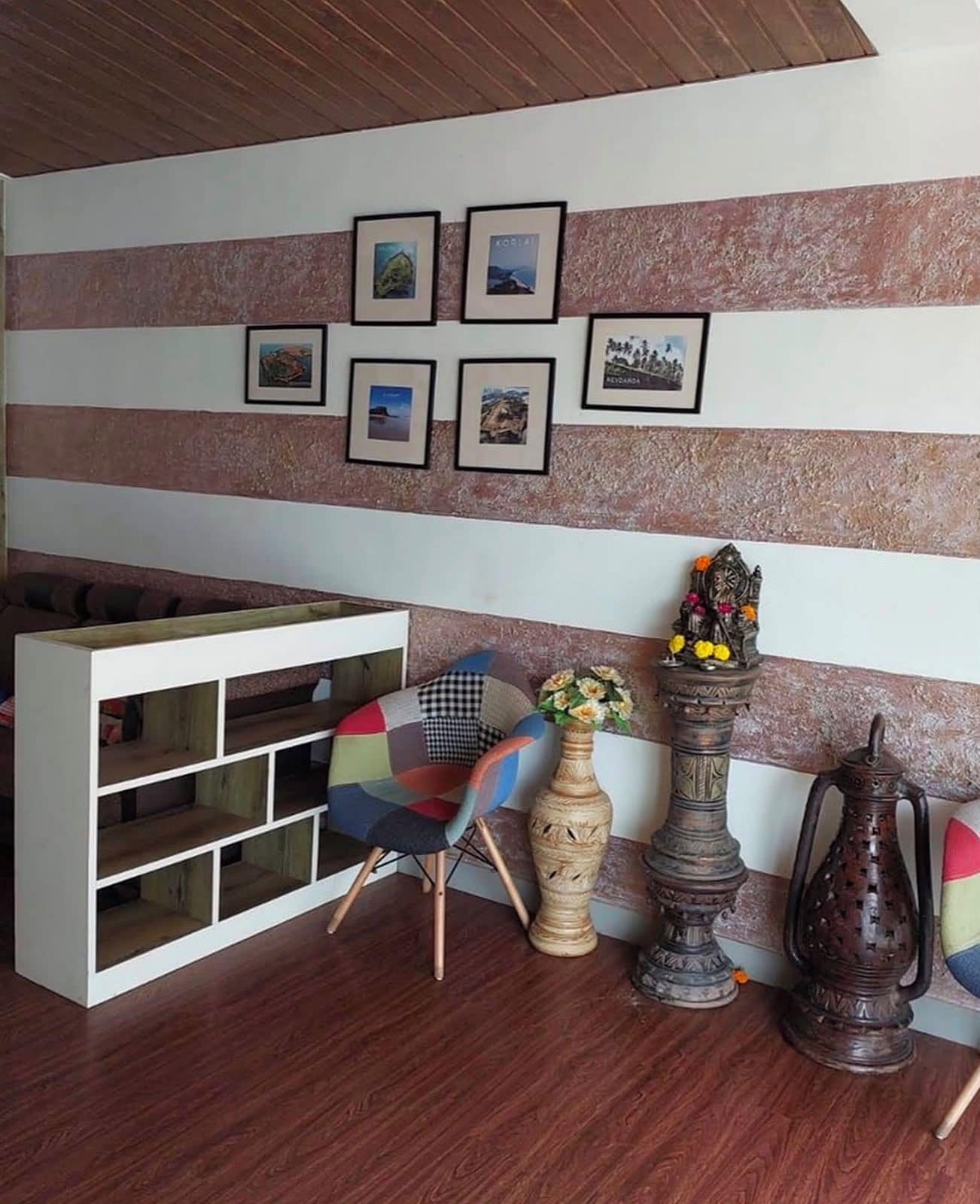A room with a wooden floor, a white shelving unit, a colorful chair, a decorative vase, and a wall with framed pictures.