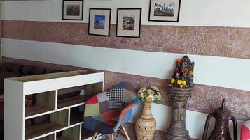 A room with a wooden floor, a white shelving unit, a colorful chair, a decorative vase, and a wall with framed pictures.