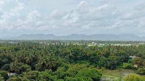 A landscape with a dense forest, scattered buildings, and distant mountains under a cloudy sky. - Lotus - The Beach Resort  (Nagaon)
