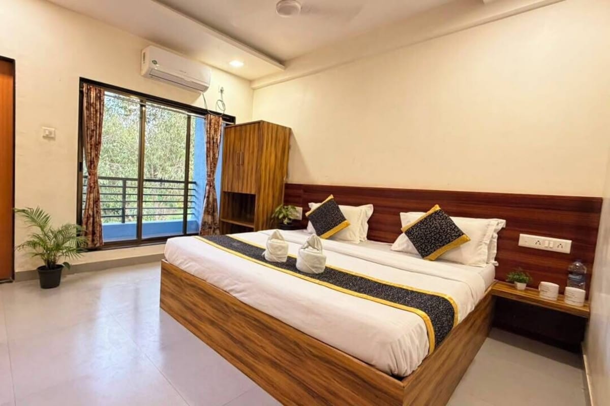 Una habitación de hotel con una cama grande, una ventana con cortinas, un cabecero de madera y una mesita de noche pequeña con una planta.