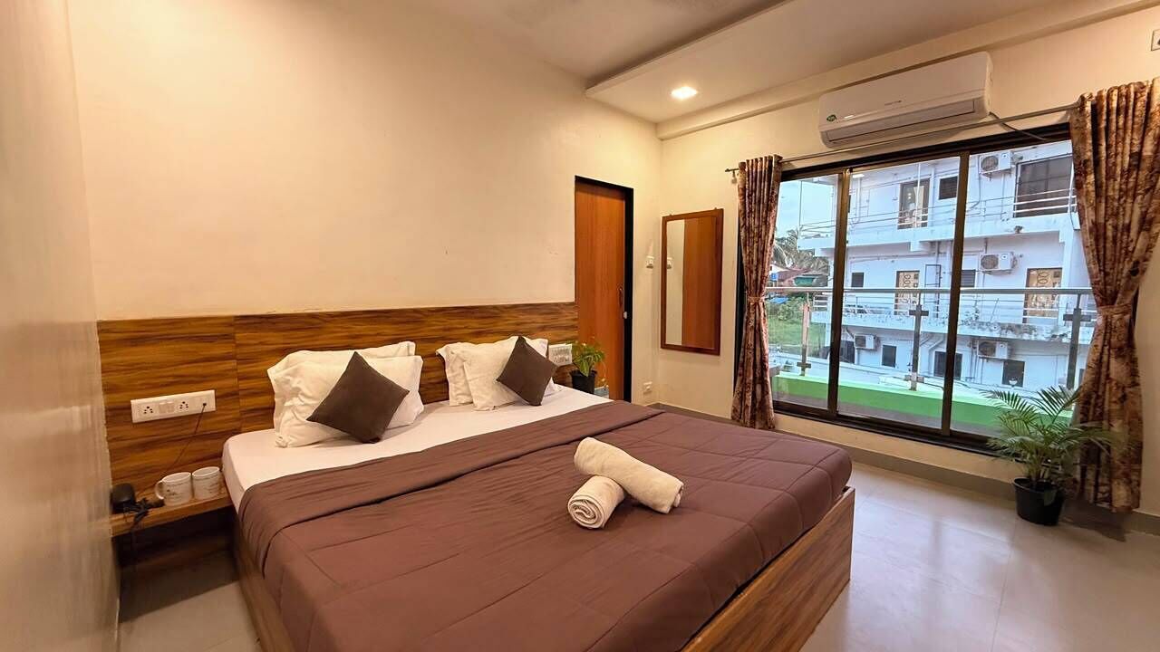 Una habitación de hotel con cama, ventana con cortinas, una planta en maceta y un equipo de aire acondicionado.
