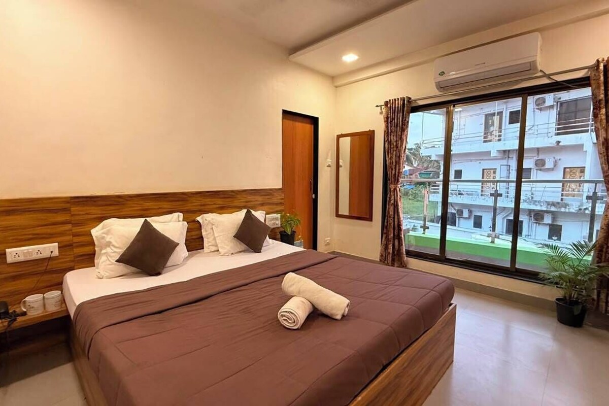 A hotel room with a bed, a window with curtains, a potted plant, and an air conditioning unit.