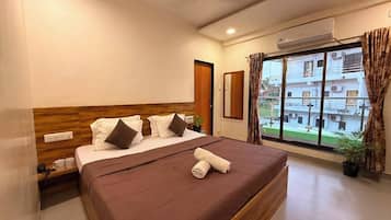 Una habitación de hotel con cama, ventana con cortinas, una planta en maceta y un equipo de aire acondicionado.