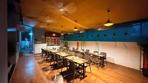 A dining area with wooden flooring, tables, chairs, and hanging pendant lights. - Lotus - The Beach Resort  (Nagaon)