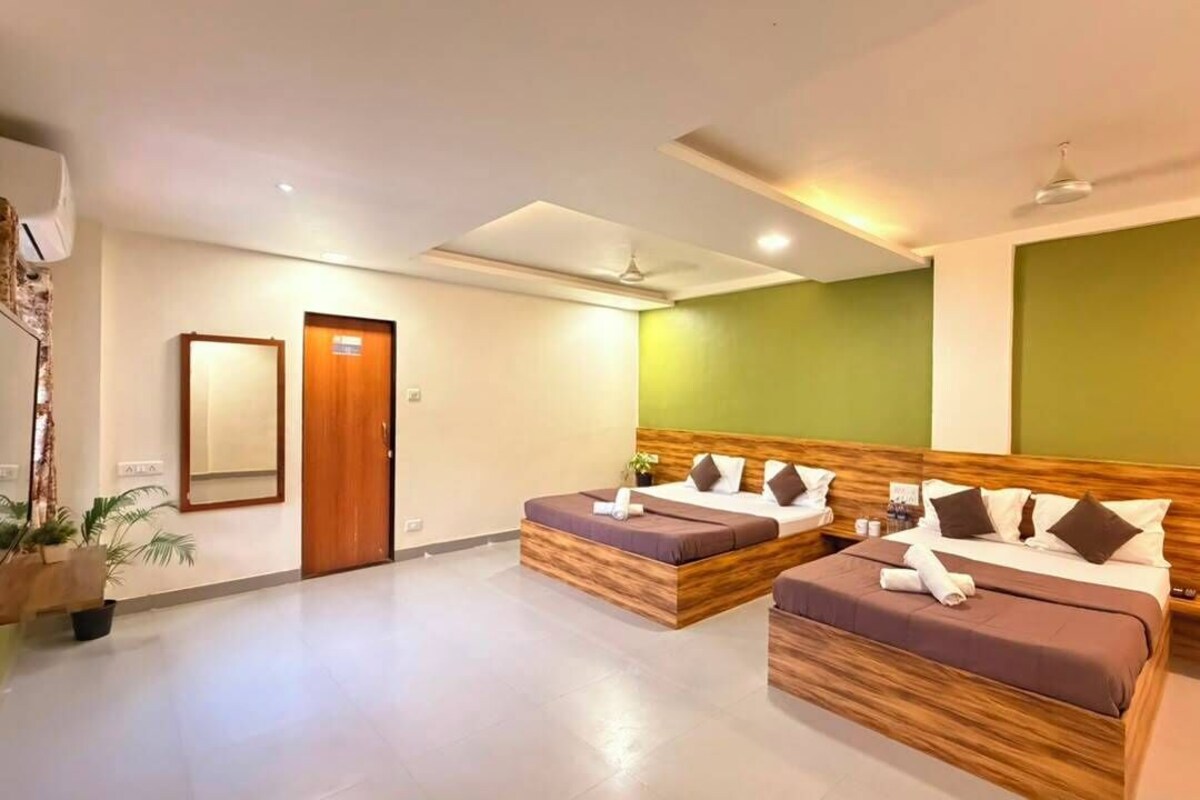 A hotel room with two beds, a wooden headboard, a green accent wall, and a ceiling fan.