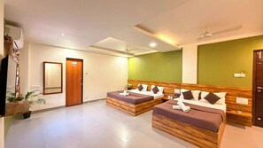 A hotel room with two beds, a wooden headboard, a green accent wall, and a ceiling fan. - Lotus - The Beach Resort  (Nagaon)