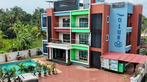 A multi-story hotel with a swimming pool, a covered outdoor area, and a vehicle parked in front. - Lotus - The Beach Resort  (Nagaon)