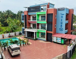 A multi-story hotel with a swimming pool, a covered outdoor area, and a vehicle parked in front. - Lotus - The Beach Resort  (Nagaon)