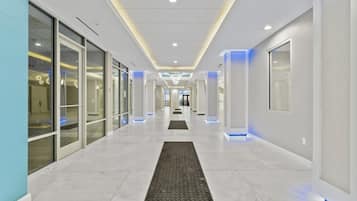 A modern hotel corridor with glass doors, recessed lighting, and a marble floor.