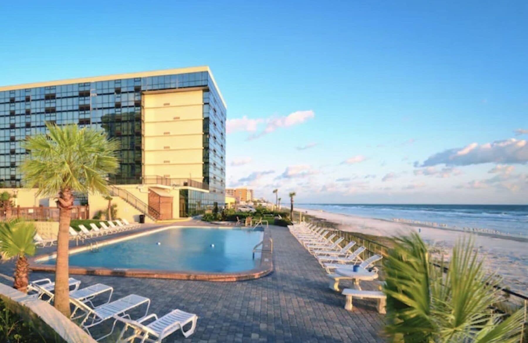 Ein modernes Hotel mit Poolbereich, Liegestühlen und Blick auf den Strand.