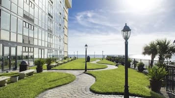 A hotel with a paved pathway, green lawns, and a view of the sea.