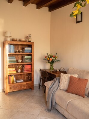 Ein gemütliches Wohnzimmer mit einer Holzbücherreol, einem Esstisch mit Blumenvase und einer Couch mit Kissen.