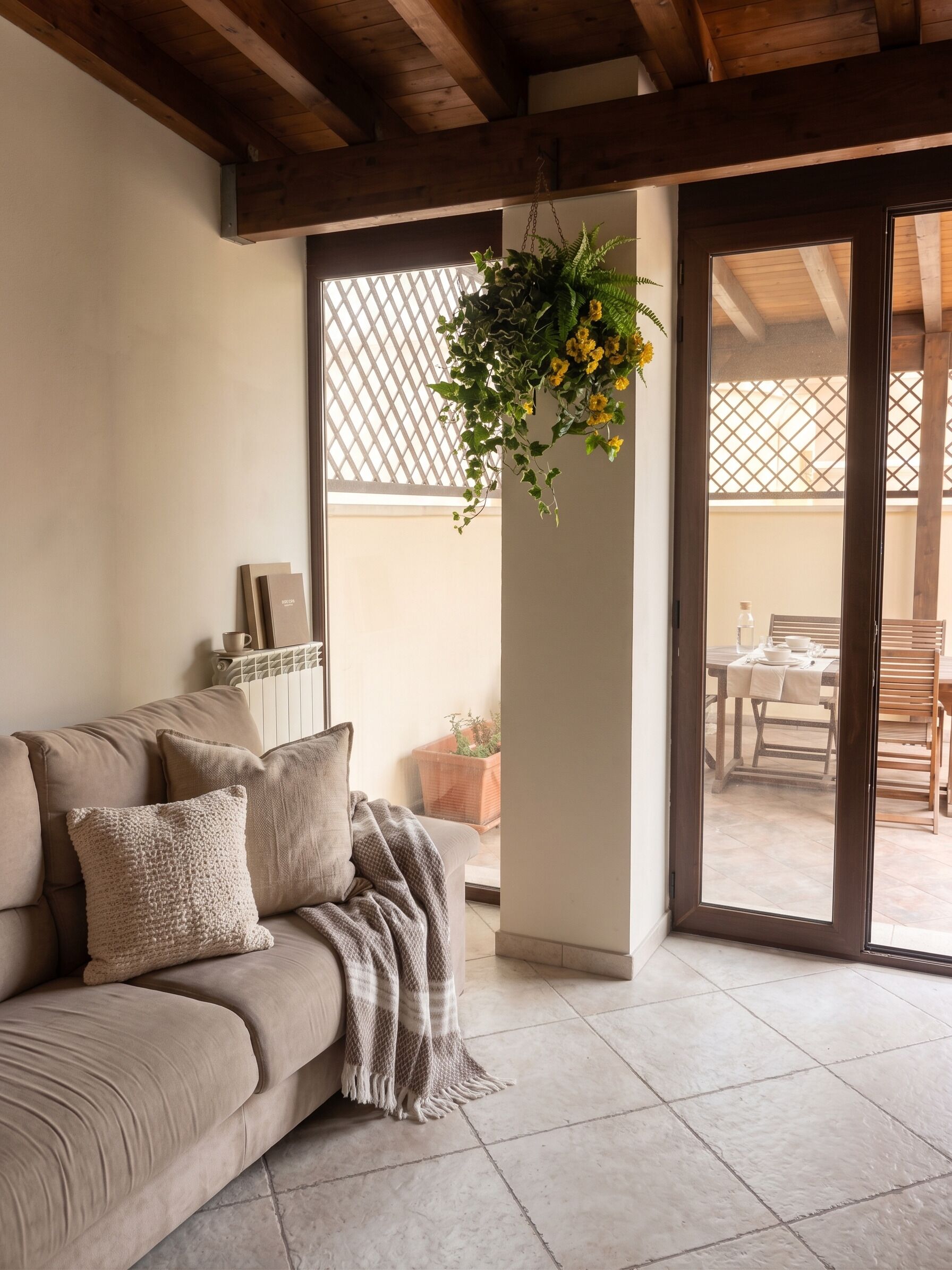 Un salon moderne avec un canapé beige, une plante suspendue et une vue sur la terrasse extérieure.
