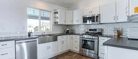 A modern kitchen with white cabinets, stainless steel appliances, and a wooden floor.
