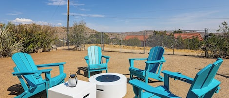 Outdoor seating with chairs and a table, surrounded by a fence and vegetation.