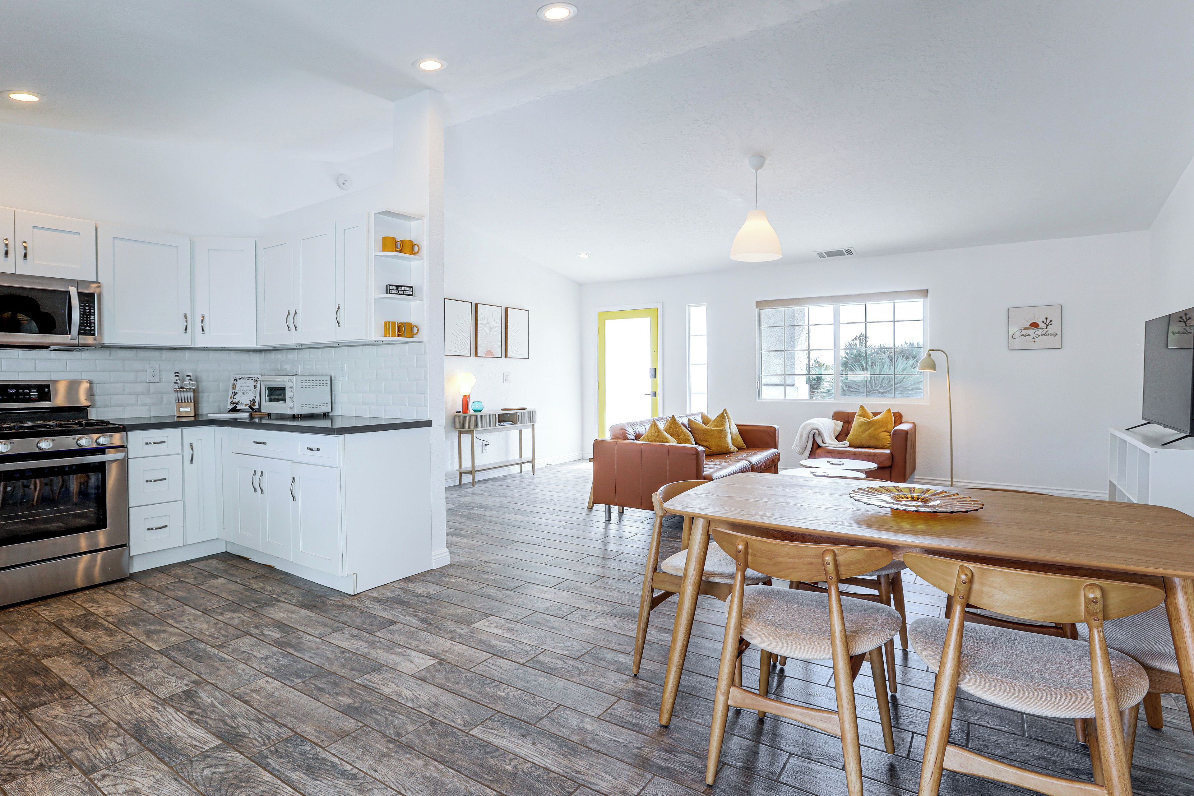 A modern kitchen with white cabinetry, a dining area with a wooden table and chairs, and a living space with a brown leather sofa.