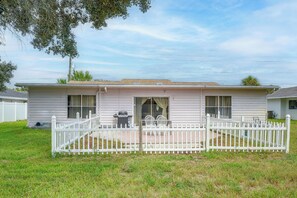 A single-story mobile home with a white picket fence, a patio with outdoor furniture, and a clear sky. - Golf, Beach, Parks! Palm Coast Family Home w/ Yard (Palm Coast)