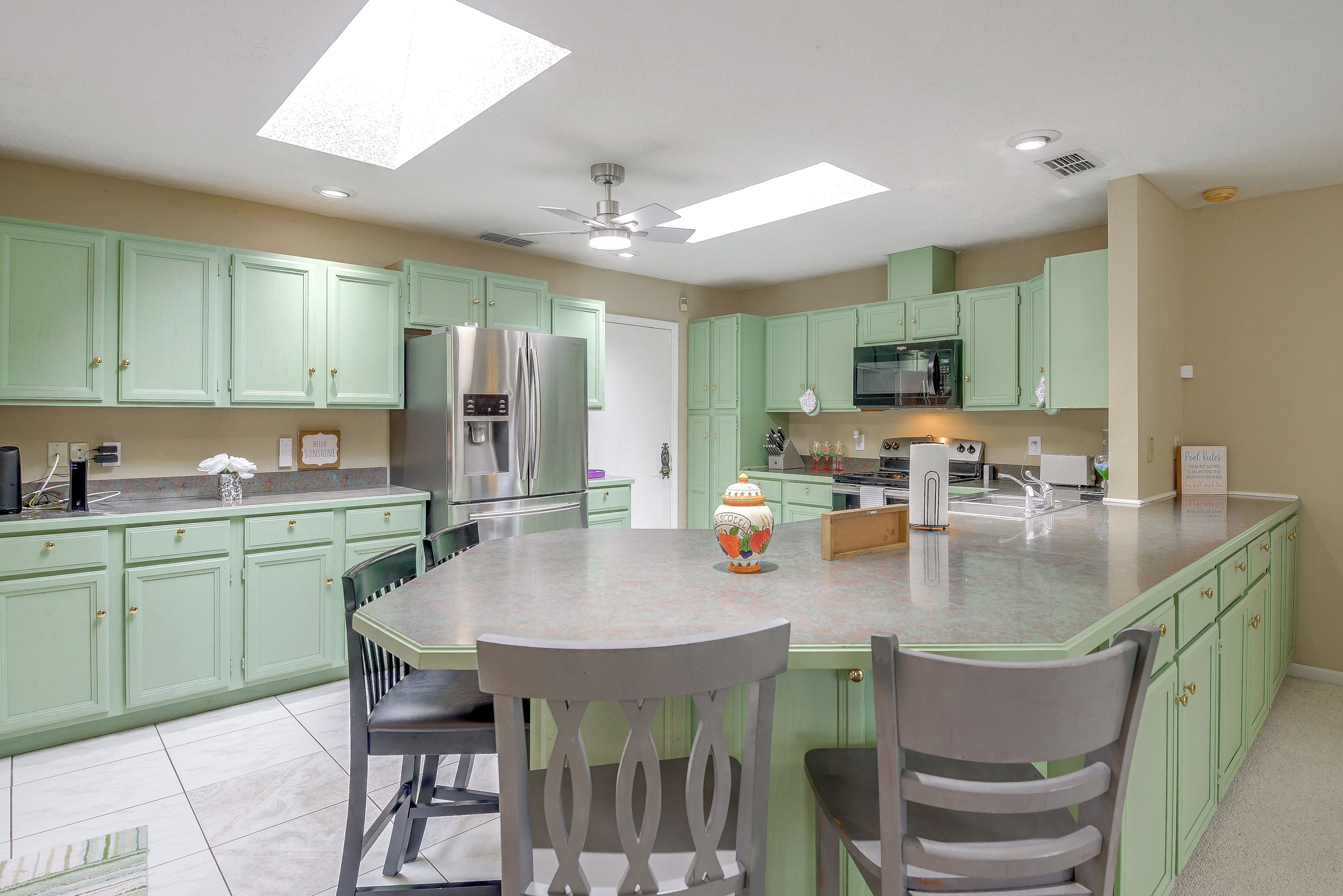 A kitchen with green cabinets, stainless steel appliances, and a central island with chairs.