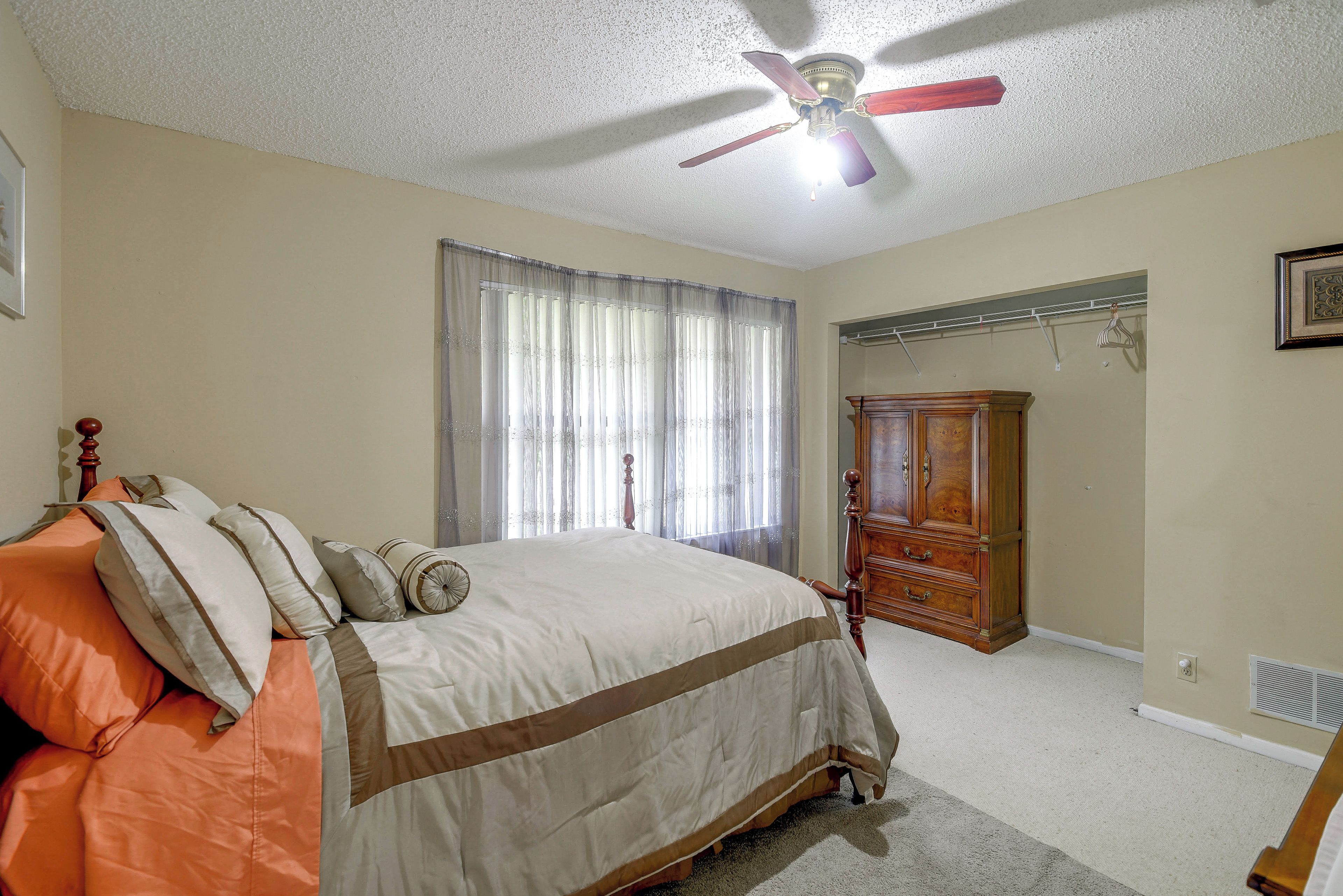 A bedroom with a bed, a ceiling fan, a wardrobe, and a window with curtains.
