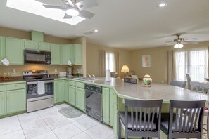 A kitchen with green cabinets, a microwave, an oven, a dishwasher, a dining table with chairs, and a ceiling fan. - Golf, Beach, Parks! Palm Coast Family Home w/ Yard (Palm Coast)