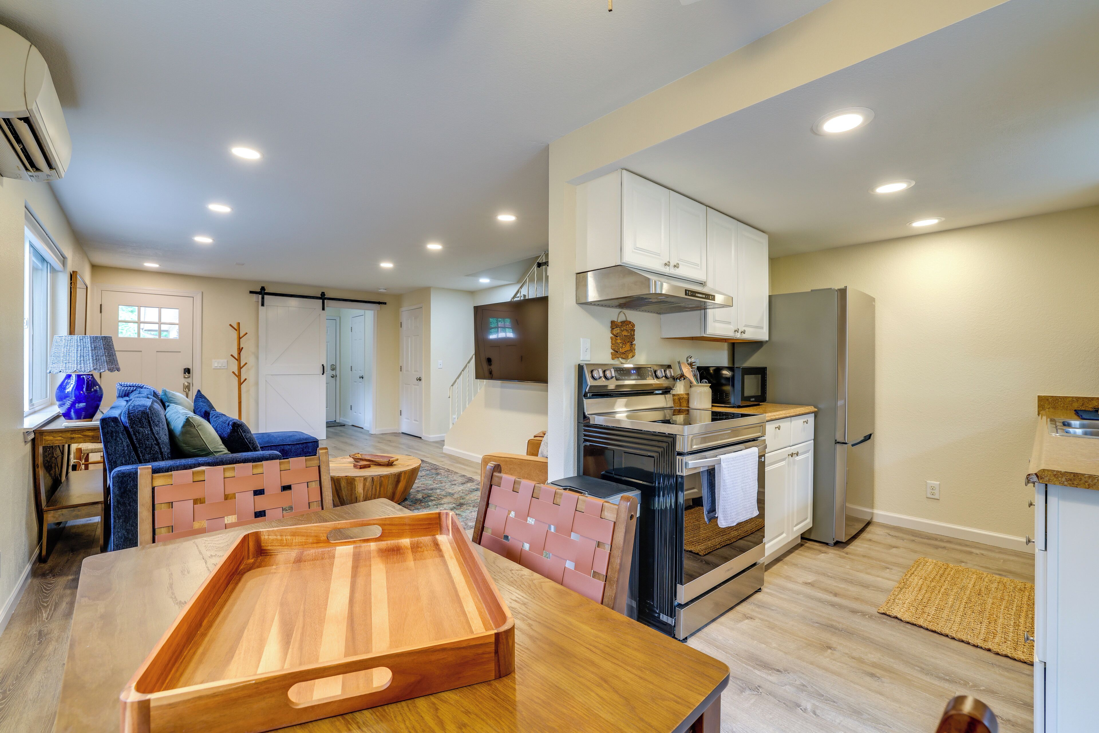 Una cocina moderna con estufa, horno y refrigerador, un comedor con mesa y sillas de madera, y una sala de estar con sofá y televisor.