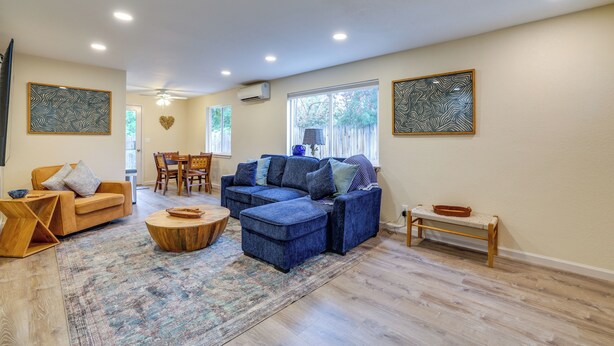 Uma sala de estar ampla com sofá azul, mesa de centro de madeira e um espaço de jantar com cadeiras e mesa.
