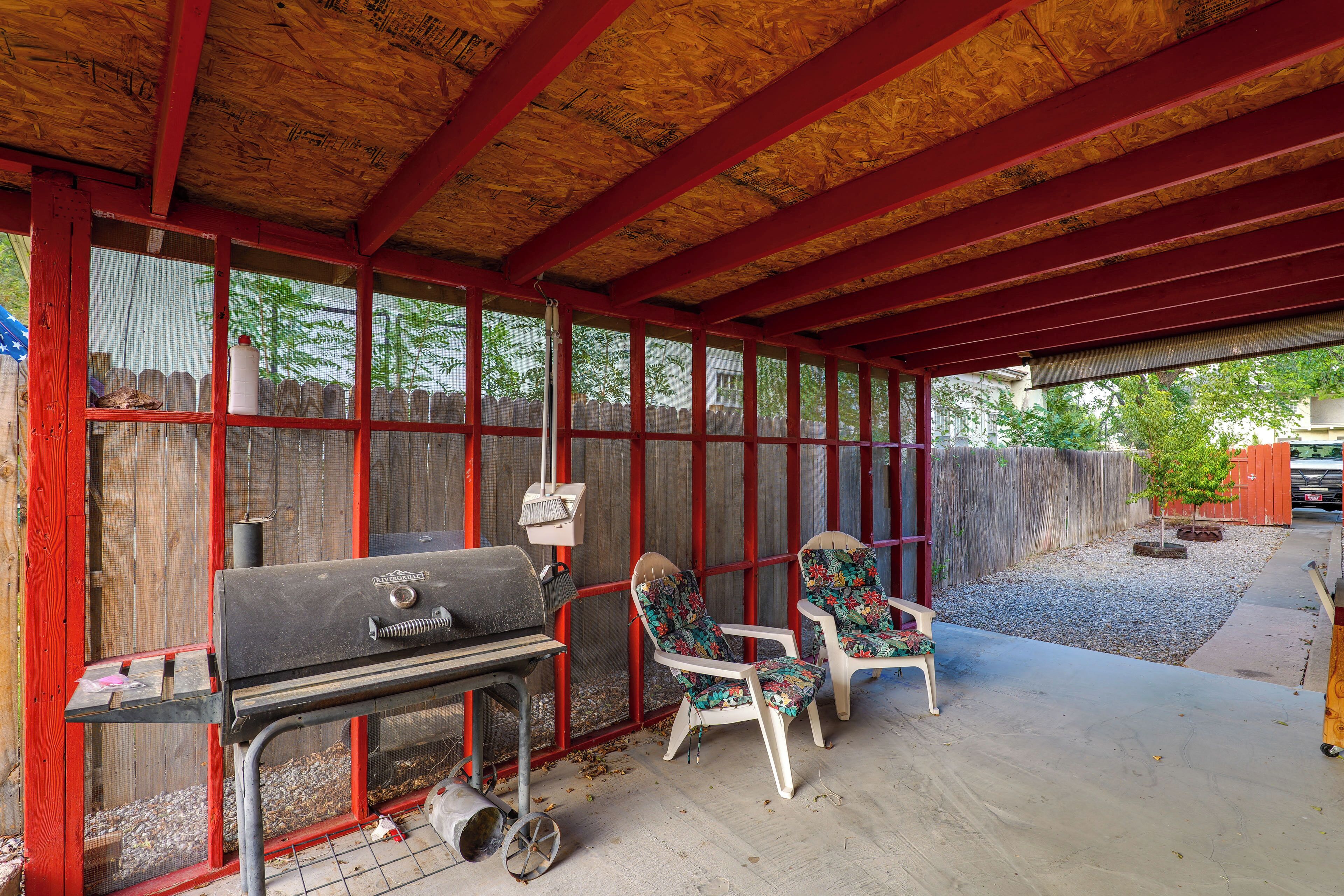 An outdoor covered patio with a grill, two chairs, and a wooden fence.