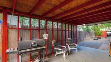 An outdoor covered patio with a grill, two chairs, and a wooden fence.