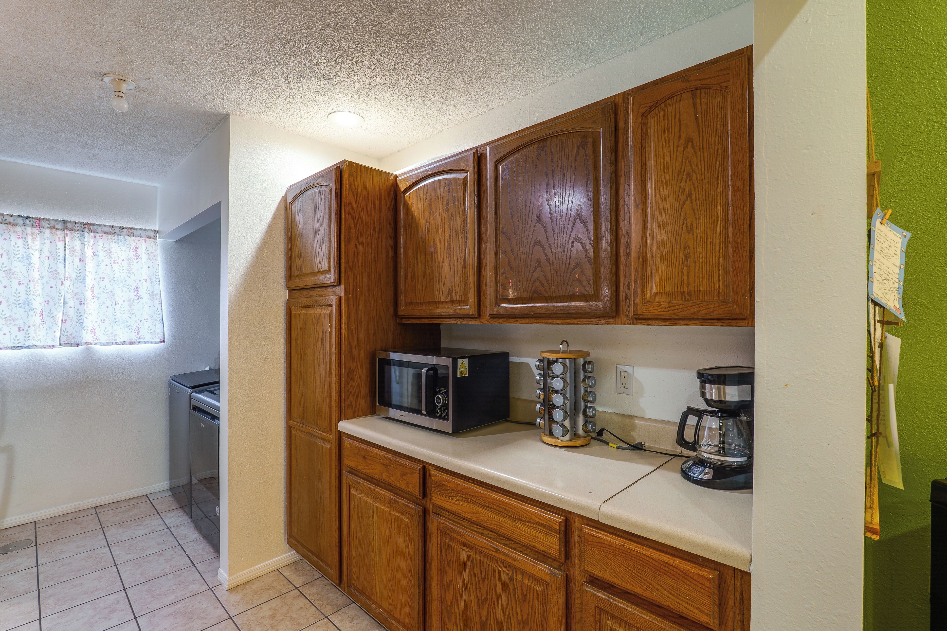 A kitchen with wooden cabinets, a microwave, a coffee maker, and a window with floral curtains.