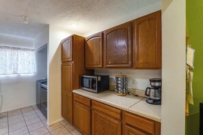 A kitchen with wooden cabinets, a microwave, a coffee maker, and a window with floral curtains.