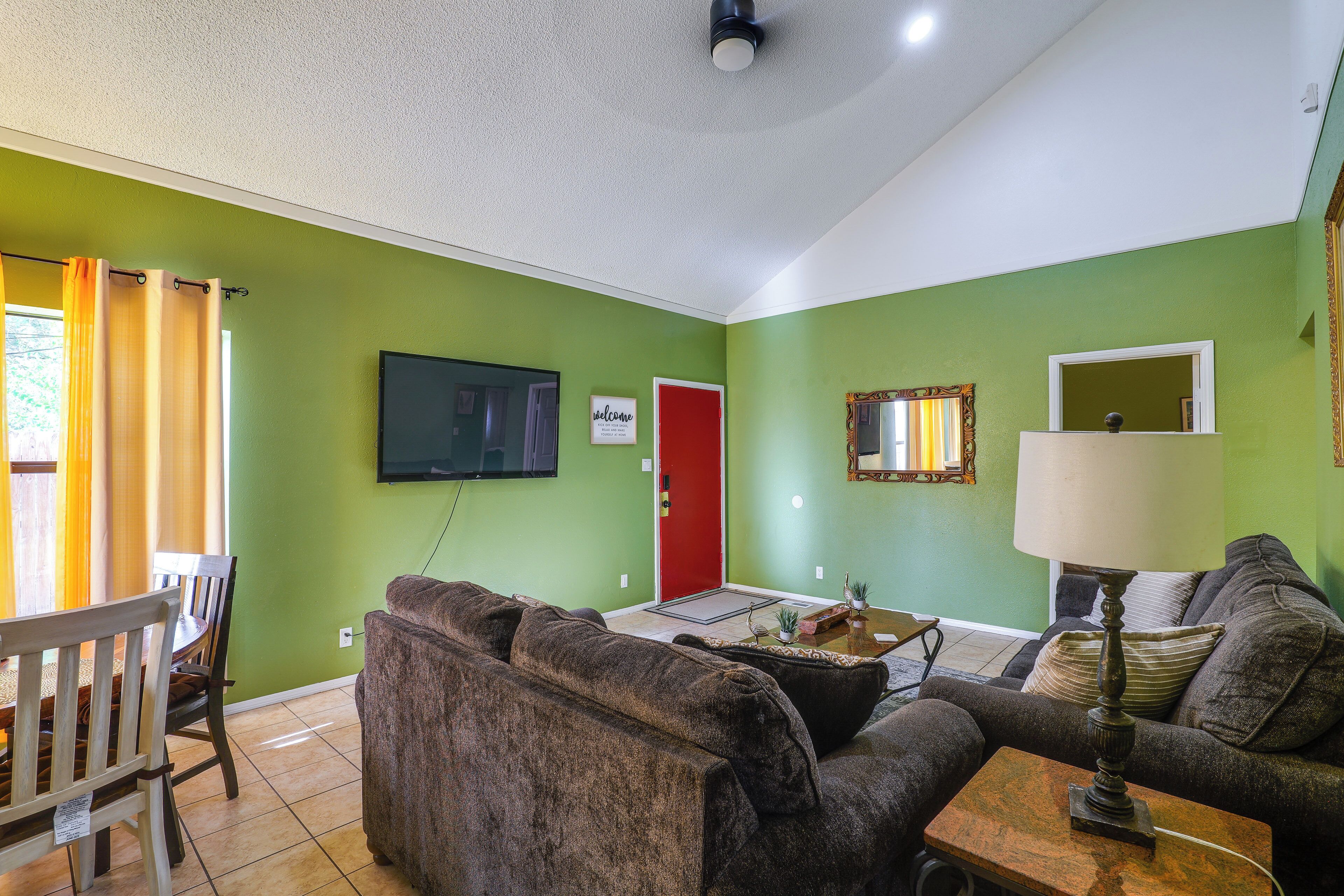 Una sala de estar con una pared verde, un televisor de pantalla plana sobre una puerta roja, un sofá, una mesa de centro y una lámpara.