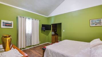 A room with a bed, a television mounted on the wall, a window with curtains, and a framed picture on the wall.
