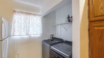 A compact kitchen with a refrigerator, stove, and a window with floral curtains.
