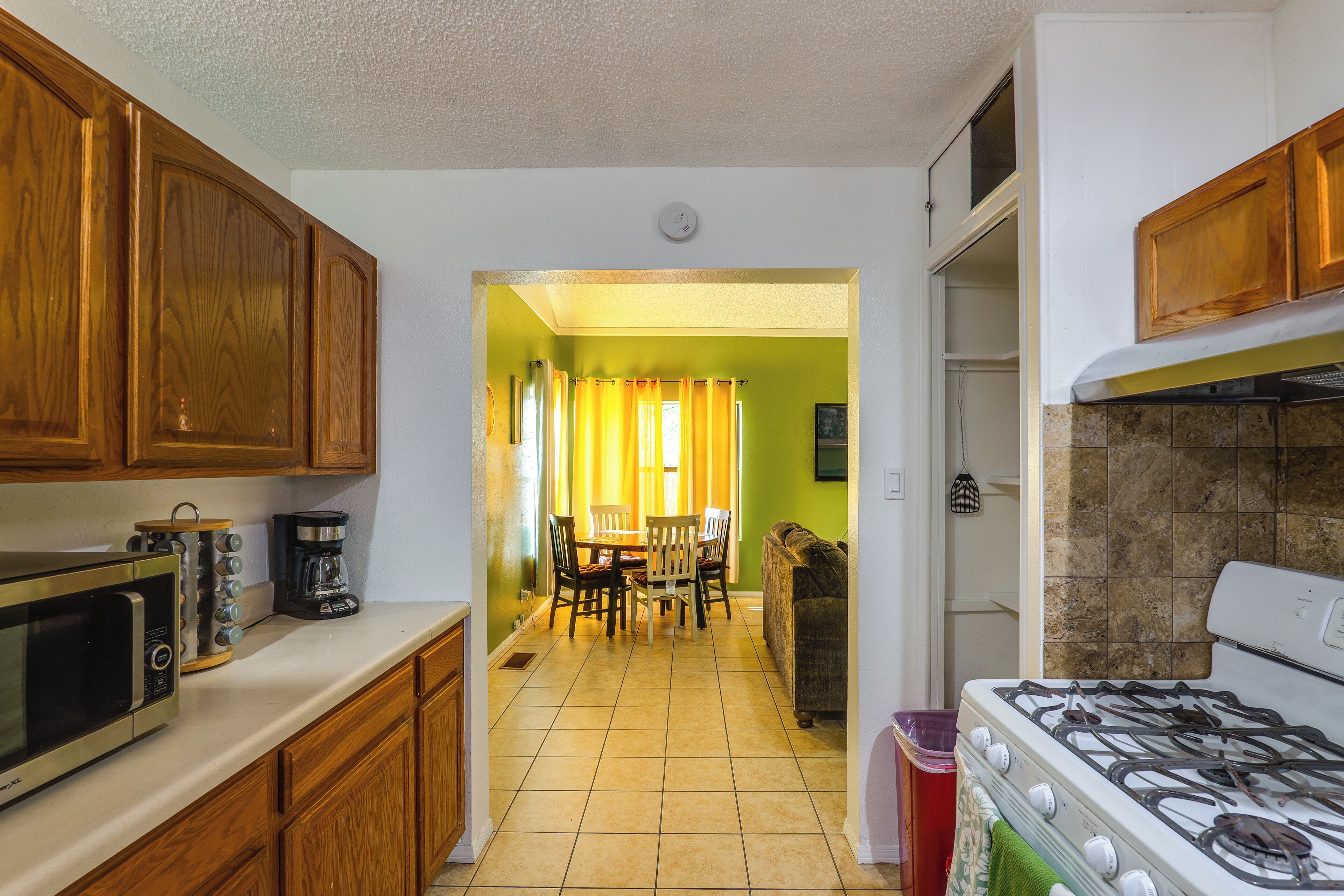 A kitchen with wooden cabinets, a stove, a microwave, and a dining area with a table and chairs.