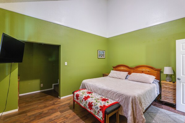 A bedroom with a bed, a bench, a bedside table with a lamp, and a wall-mounted TV.