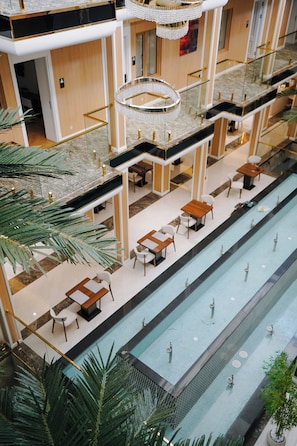 A multi-level indoor swimming pool area with multiple seating areas and a central water feature. - Unique Hotel Bukhara (Bukhara)