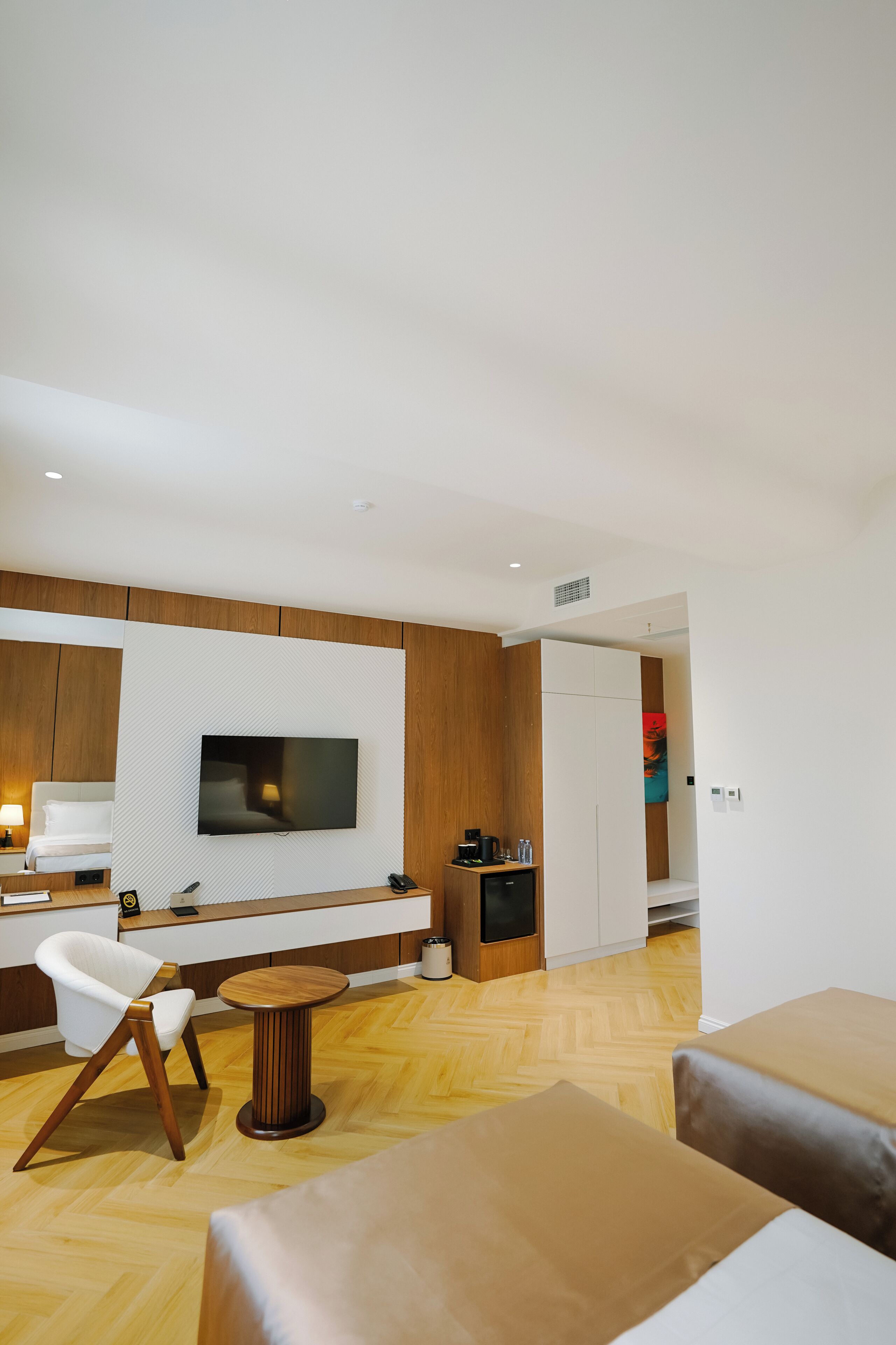 Ein modernes Hotelzimmer mit einem wandmontierten Flachbildfernseher, Holzboden, einem runden Couchtisch und einer Couch.