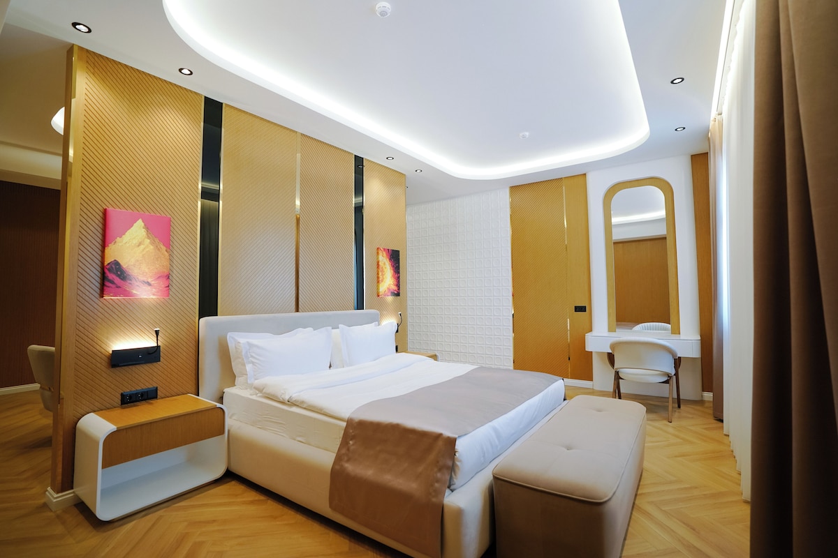 A modern hotel room with a large bed, bedside tables, a desk, and a mirror.