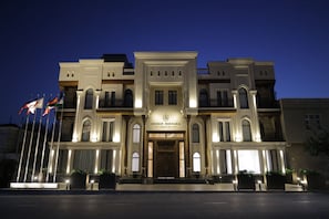 A multi-story hotel with a grand entrance, multiple flags, and a well-lit facade. - Unique Hotel Bukhara (Bukhara)