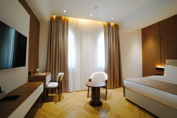 A modern hotel room with a bed, a desk, a chair, a small table, and a TV.