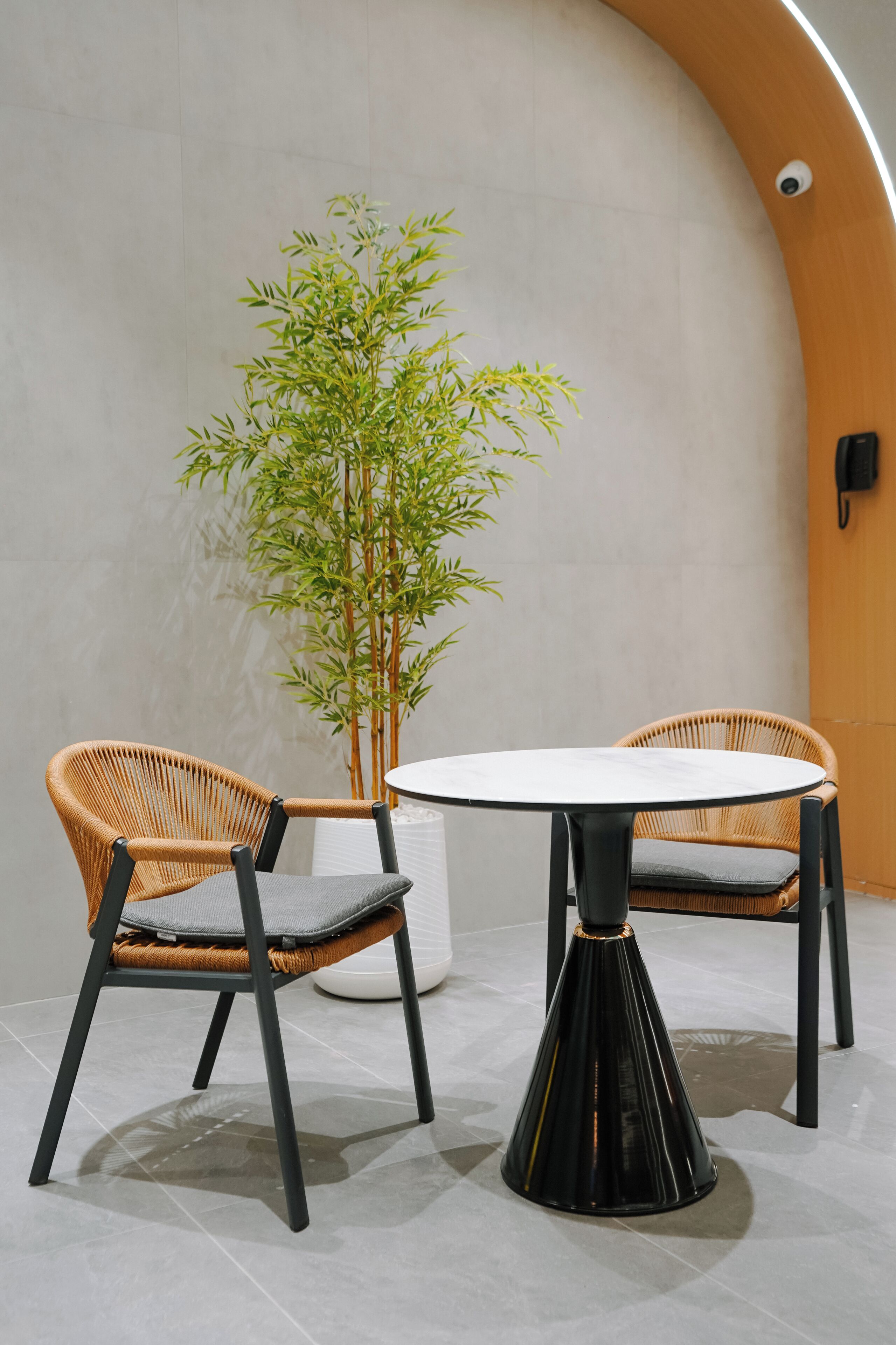 Un interior moderno con dos sillones de mimbre, una mesa de mármol blanco y una planta de bambú.