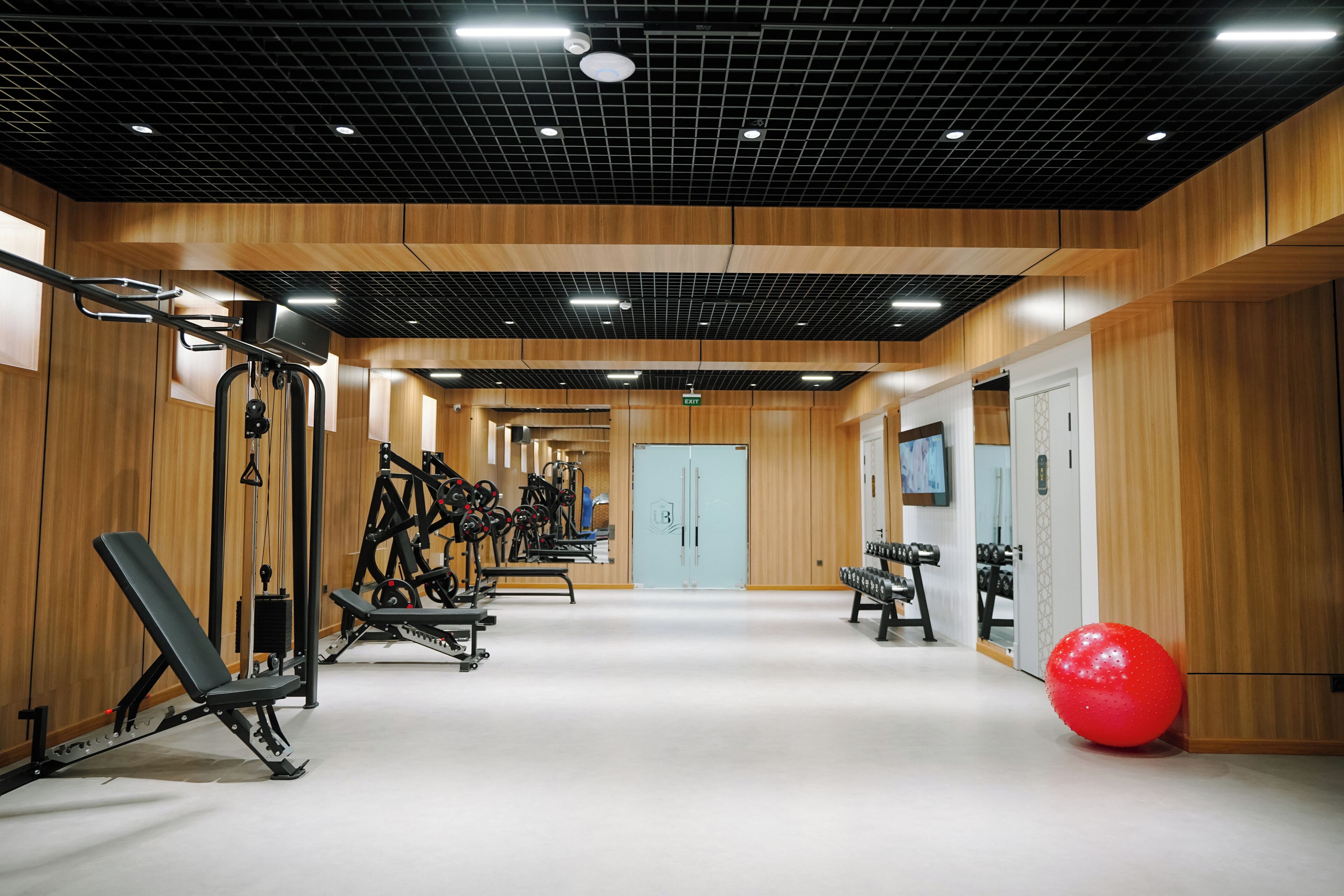 Un gimnasio con equipo de ejercicios, una pelota roja y paredes de madera.