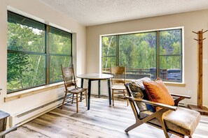 Una habitación con ventanas amplias, una mesa redonda, dos sillas y un sofá con cojines.