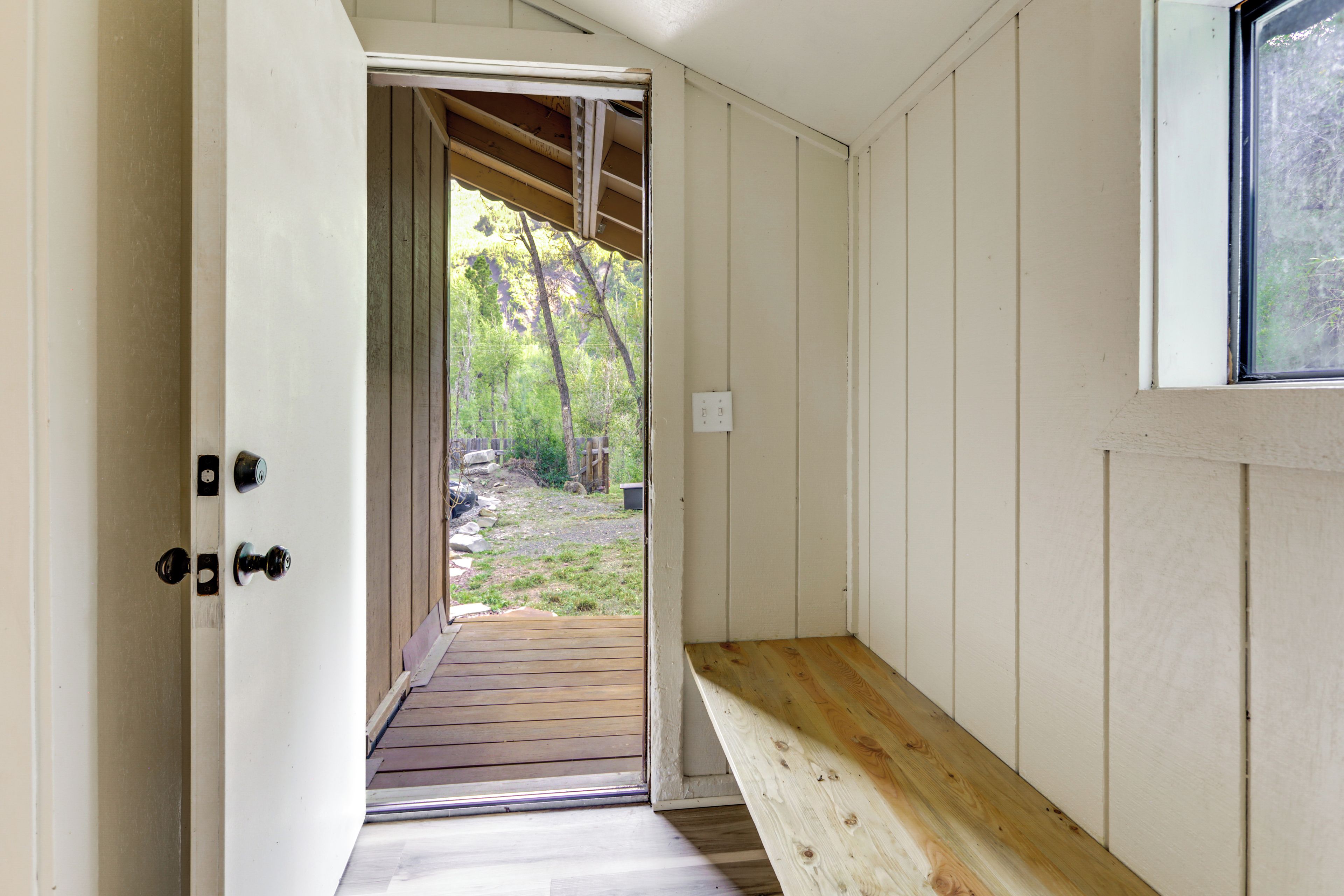 An interior hallway with a wooden bench, a door leading outside, and a window.
